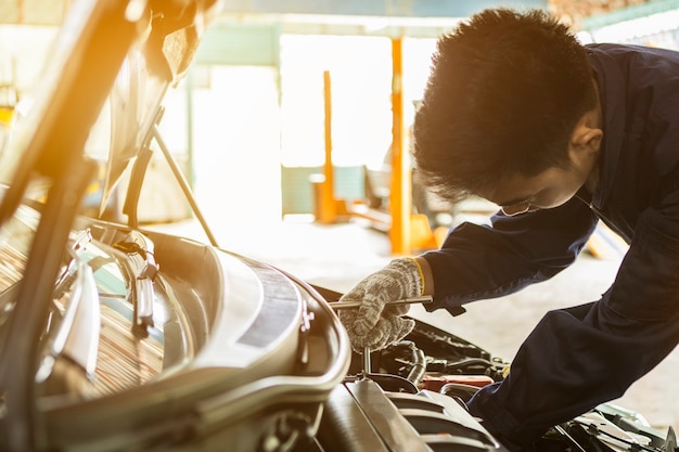 Azjatyckiego mężczyzna auto mechanik używa śrubokręt i wyrwanie pracować usługowego samochód w garażu.