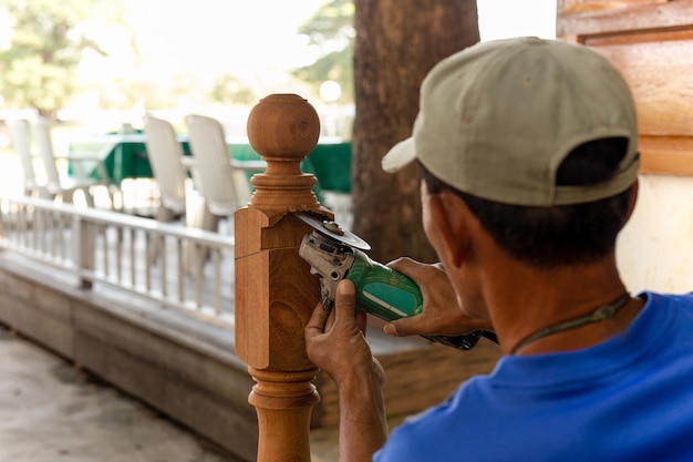 Azjatyckiego pracownika rżnięty drewniany słup z szlifierską maszyną plenerową.