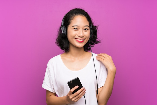 Azjatyckiej młodej dziewczyny słuchająca muzyka z wiszącą ozdobą nad odosobnioną purpury ścianą