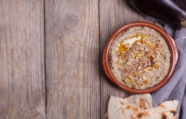 Baba ganoush Przystawka kuchni lewantyńskiej z pieczonego bakłażana i pasty sezamowej z oliwą z oliwek, przyprawami, ziołami i orzechami włoskimi, lawasz na drewnianym tle z serwetką. Skopiuj miejsce