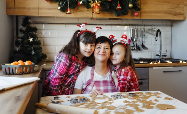Babcia i dwie wnuczki przytulają się w kuchni w wigilię Bożego Narodzenia. Codzienny styl życia we wnętrzu z prawdziwego życia.