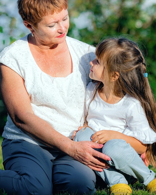 Babcia I Wnuczka Siedzą Na Trawniku W Letni Dzień Mała Dziewczynka Uważnie Słucha Babci