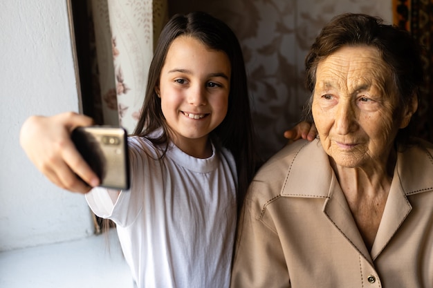 Babcia i wnuczka. Śliczna mała dziewczynka pokazuje swojej babci smartfon.