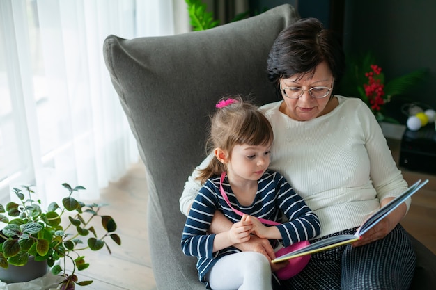 Babcia przytula swoją małą wnuczkę, czyta jej książkę. Babcia opowiadająca historie małej dziewczynce.