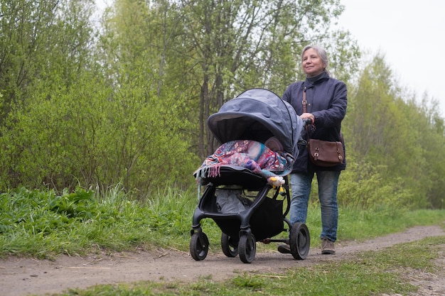 Babcia spacerująca po wiosennym parku miejskim z wnukiem z noworodkiem w wózku