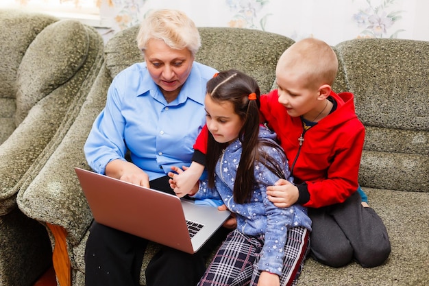 Babcia z wnukami korzysta z laptopa w domu