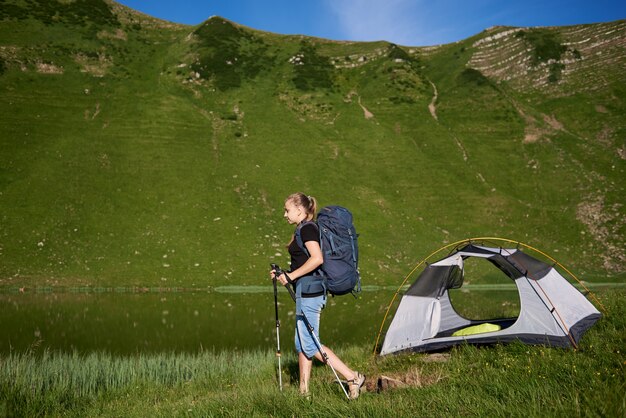 Backpacker Kobieta Z Plecakiem I Kije Trekkingowe W Pobliżu Namiotu, Ciesząc Się Letni Dzień W Pobliżu Jeziora W Górach