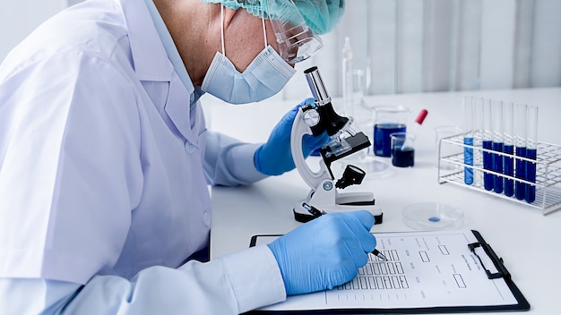 Badacz medyczny lub naukowy lub lekarz mężczyzna patrzący na probówkę z klarownym roztworem w laboratorium