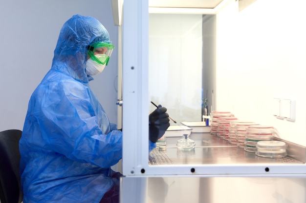 badaczka nauk ścisłych w mundurze ochronnym i sprzęcie pracuje z płytką Petriego w laboratorium