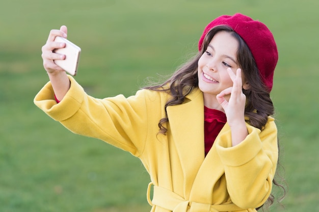 Bądź na bieżąco Szczęśliwy mały bloger prowadzi wideoblog lub vlog Śliczna dziewczyna pokazuje ok gest dla zdjęcia na blogu Małe dziecko robi selfie na nowy blog na zewnątrz Blog na żywo Blog na żywo w czasie rzeczywistym