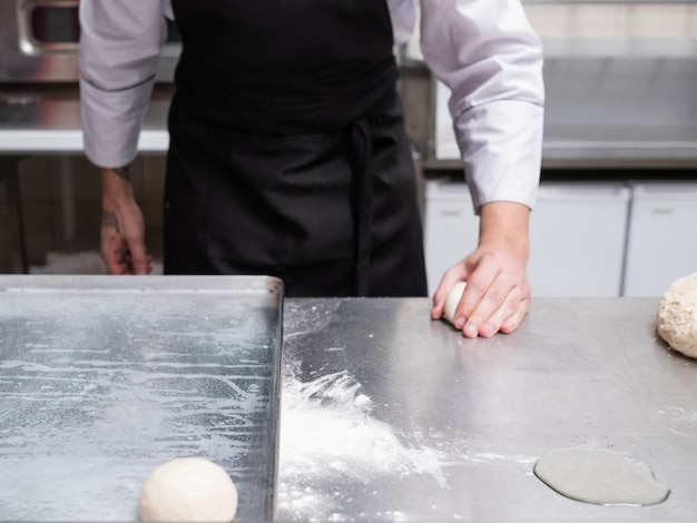 Baker pracuje z ciastem na metalowej powierzchni roboczej. Profesjonalny kucharz robi bułki lub bułki