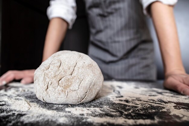 Baker ugniata ciasto na czarnym stole i kładzie ręce na stole