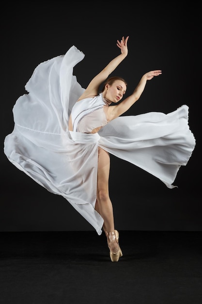 Zdjęcie balerina w białej sukience i butach pointe stoi na palcach i tańczy na czarnym tle