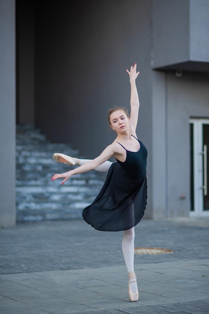 Balerina w tutu pozuje na tle budynku mieszkalnego Piękna młoda kobieta w czarnej sukience i pointe tańcząca balet na zewnątrz