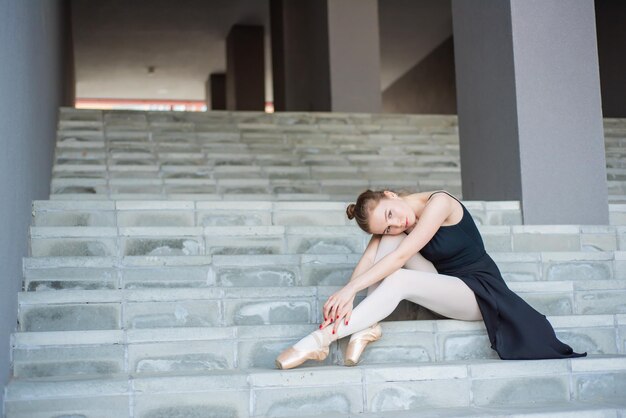 Balerina w tutu pozuje siedząc na schodach Piękna młoda kobieta w czarnej sukience i pointe odpoczywa siedząc w eleganckiej pozie na schodach z zewnątrz