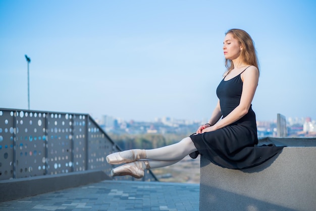 Balerina w tutu pozuje siedząca Piękna młoda kobieta w czarnej sukience i pointe tańcząca na tle miasta Portret wspaniałej baletnicy wykonującej taniec na świeżym powietrzu