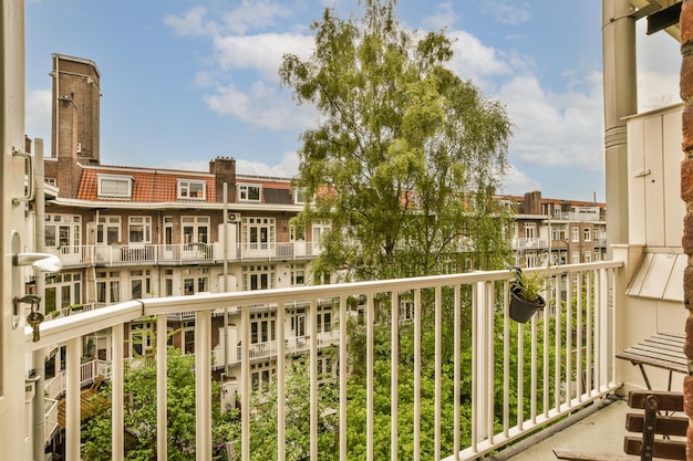 Balkon z białą balustradą i zielonymi drzewami na pierwszym planie, wzięty z okna apartamentowca