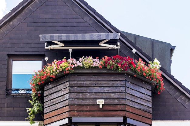 Balkon z kwiatami. Balustrady drewniane balkonowe i baldachim tekstylny na elewacji drewnianego domu.