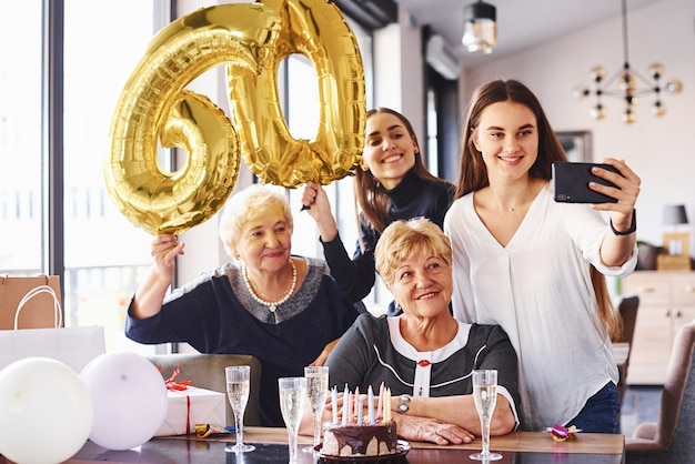 Balony z numerem 60. Senior kobieta z rodziną i przyjaciółmi świętuje urodziny w pomieszczeniu.