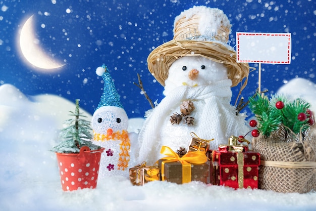 Bałwan w zaspie z prezentami i choinkami i czeka na Świętego Mikołaja. Pocztówka koncepcyjna na Boże Narodzenie i Nowy Rok.