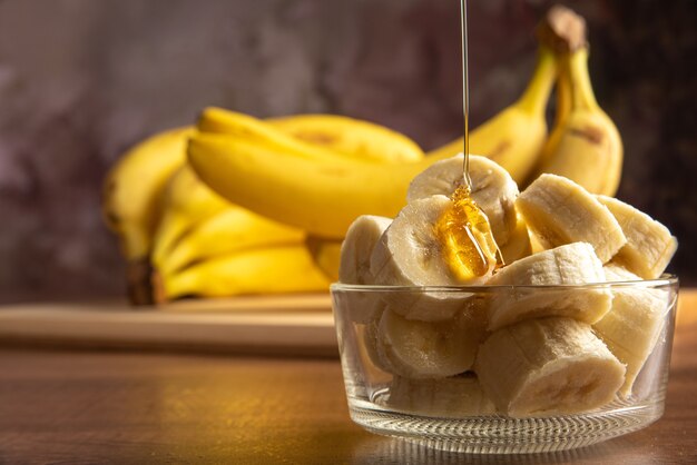 Banan Pokrojony W Plasterki W Szklanym Słoju Skąpanym W Miodzie Z Większą Ilością Bananów W Tle, Ciemne Tło Abstrakcyjne, Selektywna Ostrość.