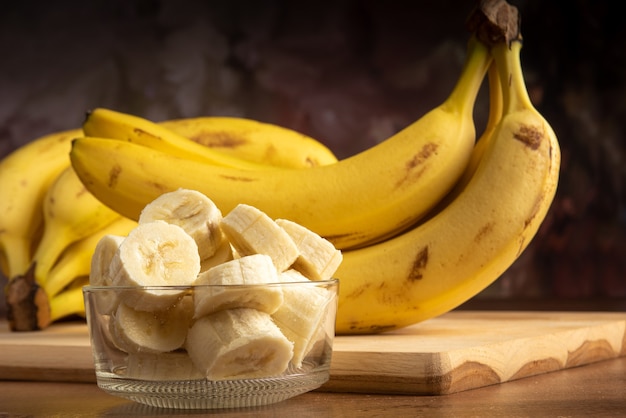Banan pokrojony w plasterki w szklanym słoju z większą ilością bananów w tle, ciemne tło abstrakcyjne, selektywna ostrość.