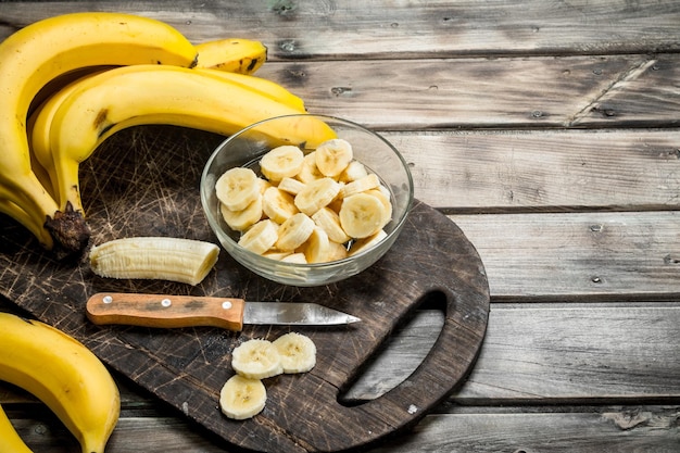 Banany i plasterki bananów w talerzu na czarnej desce do krojenia z nożem