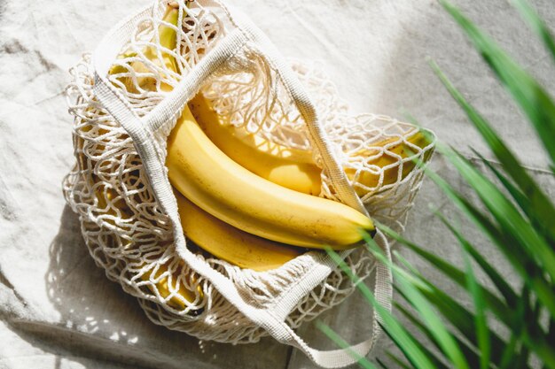 Banany w siatkowej torebce na lnianej serwetce ozdobionej liśćmi palmy Ekologiczna i letnia koncepcja