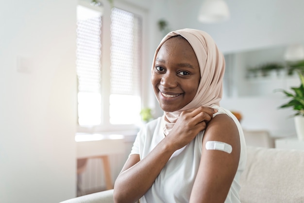 Bandaż samoprzylepny na ramieniu po wstrzyknięciu szczepionki lub leku, BANDAŻE SAMOPRZYLEPNE TYNK - Sprzęt medyczny, Soft focus Bandaż samoprzylepny na ramieniu muzułmańskiej afrykańskiej kobiety po szczepieniu Covid-19