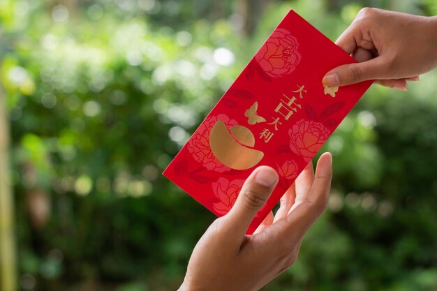 Banjarnegara styczeń 2023 Czerwony Angpao trzymany w jednej ręce z naturalnym zielonym rozmyciem tła Chiński Nowy Rok