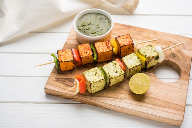 Barbecue Paneer Tikka Kabab - indyjskie kostki twarogu Tandoori w czerwonym i białym sosie w patyczkach, podane w talerzu z zielonym chutney na kolorowym lub drewnianym blacie, selektywne focus