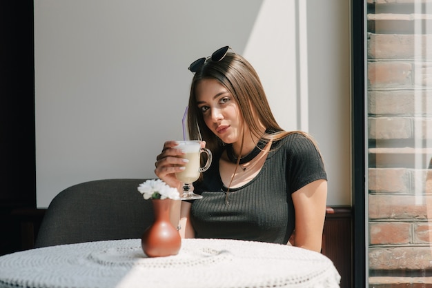 Bardzo młoda kobieta siedzi w kawiarni przy filiżance kawy latte.