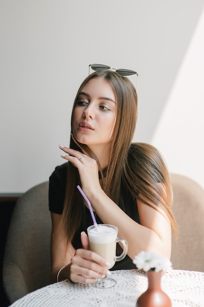 Bardzo młoda kobieta siedzi w kawiarni przy filiżance kawy latte.