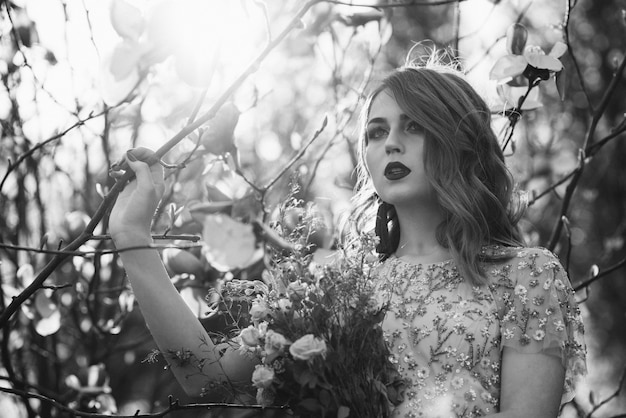 Bardzo piękna dziewczyna panna młoda pod welonem, beżowa suknia ślubna w pobliżu drzewa Sakura patrzy w dół, przyroda