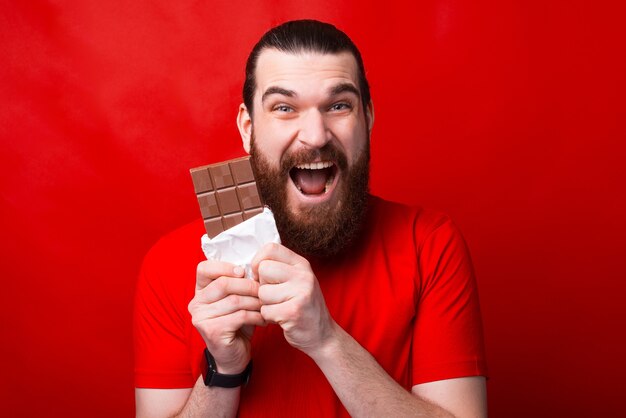 Bardzo podekscytowany mężczyzna je czekoladę przed kamerą, patrząc na nią