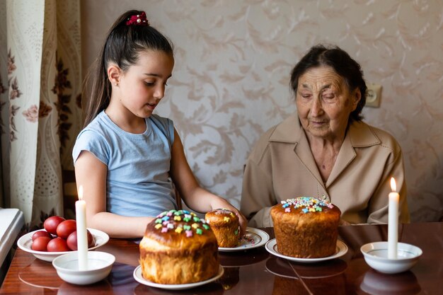 bardzo stara babcia i wnuczka kolorują jajka, przygotowując ciasto wielkanocne na Wielkanoc w domu.