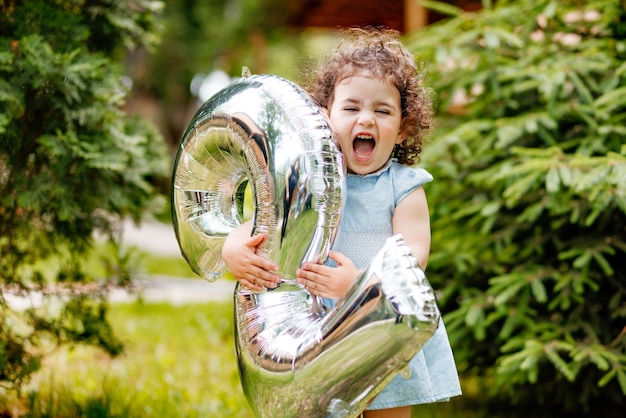 Zdjęcie bardzo szczęśliwa dwuletnia dziewczynka świętująca swoje urodziny śmiejąc się trzymając numer balonu