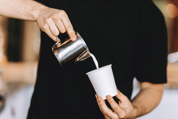 Barista ostrożnie nalewa mleko do szklanki w nowoczesnej kawiarni. .