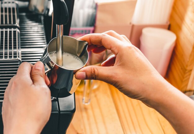 Barista używa ekspresu do kawy do mieszania świeżego mleka w pianie w kawiarni