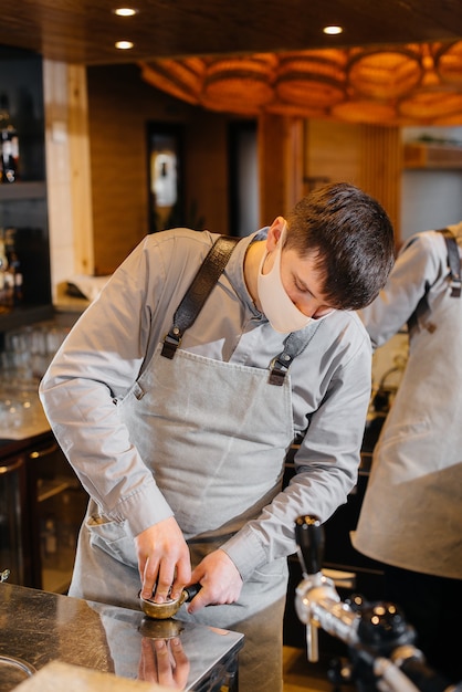 Barista w masce przygotowuje pyszną kawę przy barze w kawiarni