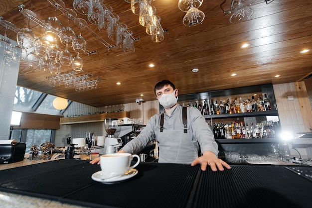 Zdjęcie barista w masce wykwintnie serwuje gotową kawę w nowoczesnej kawiarni podczas pandemii podawanie klientowi gotowej kawy w kawiarni