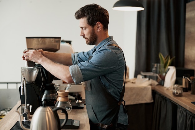 Barista wsypuje ziarna kawy do zbiornika ekspresu do kawy w celu zmielenia w kawiarni