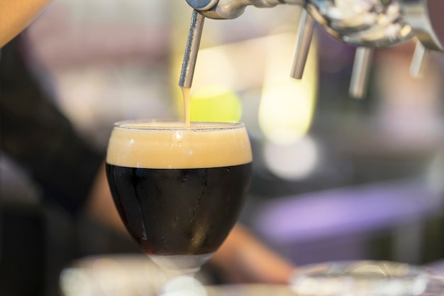 Barman leje czarne piwo w szklance.