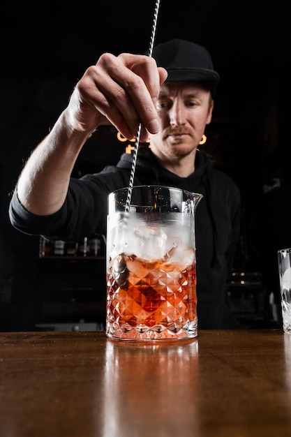 Barman miesza gin campari i słodki wermut, aby przygotować koktajl alkoholowy Negroni Barman przygotowuje tradycyjny koktajl Negroni w barze