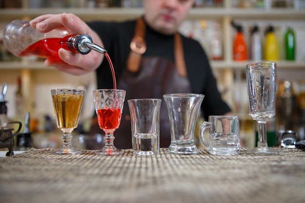 Barman nalewa różne napoje alkoholowe do małych szklanek na barze