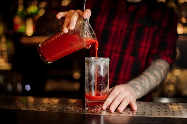 Barman nalewa świeży, słony, czerwony pomidorowy napój alkoholowy do szklanki na blacie barowym