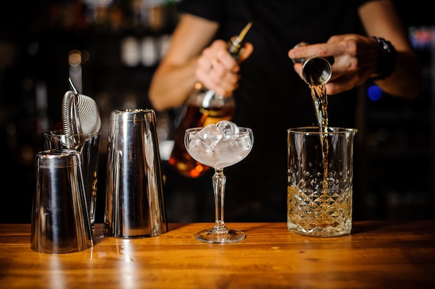 Barman przygotowuje bursztynowy koktajl alkoholowy przy użyciu kryształowego szkła z lodem