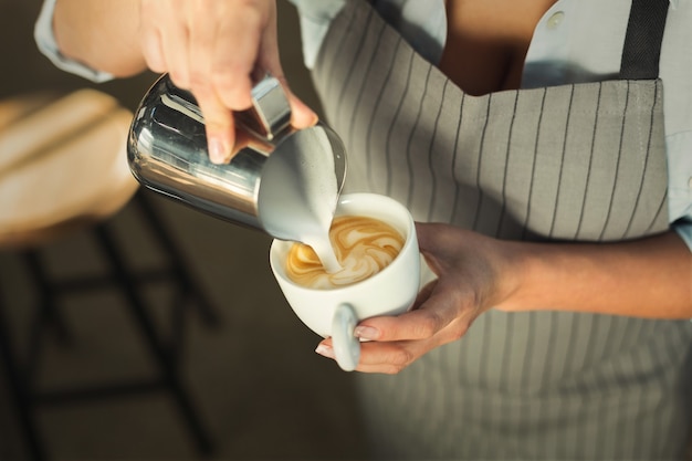 Barman robi cappuccino. Zbliżenie kobiecej dłoni wlewając gorącego mleka pianki do espresso. Latte art, mały biznes i profesjonalna koncepcja parzenia kawy