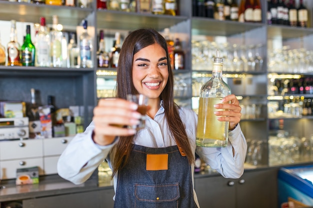 Barman trzyma kieliszek z napojem alkoholowym i butelkę w drugiej ręce