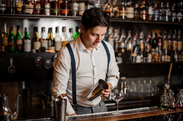 Barman w białej koszuli robi koktajl przy blacie barowym